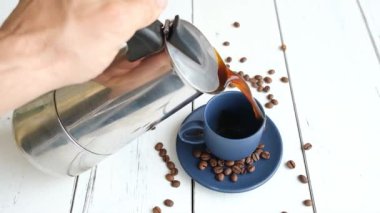 Kahveyi koyu mavi bardağa dolduran adam beyaz ahşap bir masada..