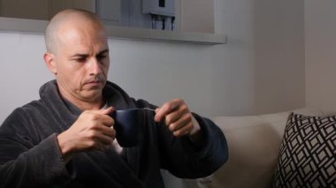 48 yaşında Brezilyalı bir adam bornoz giyiyor ve bir fincan çay içiyor ve televizyona gülümsüyor..