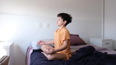 11 yaşındaki Brezilyalı çocuk yatakta oturmuş yoga yapıyor..