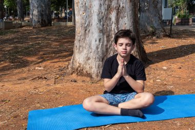 Brezilya 'lı çocuk yoga minderinde oturuyor ve açık havada nefes alma alıştırması yapıyor..