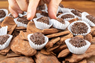 Male hand picking up a Brazilian chocolate truffle over small tree bark_18. clipart