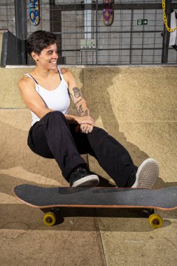 26 yaşındaki Brezilyalı kadın gülümsüyor ve ayaklarının altında kaykayla kasede oturuyor..