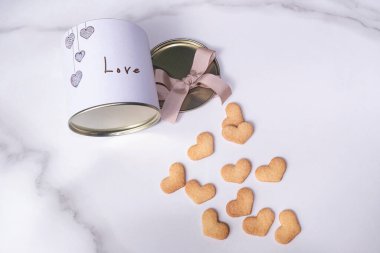 Yuvarlak beyaz bir kutunun yanında kalp şeklinde kurabiyeler.