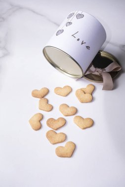 Metal kapaklı, dairesel beyaz bir kutunun yanında kalp şeklinde kurabiyeler. _ dikey.