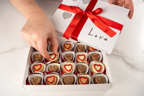 Kırmızı fiyonklu bir kutudan çikolata alan kadın..