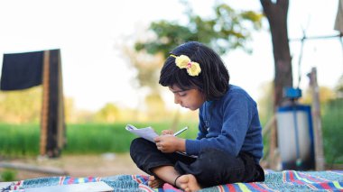 Öğrenci elinde kalemle parkta ödev yapıyor. Okul konseptine geri dönelim. Zavallı Çocuklar Yaşam Tarzı. Eğitim kavramı