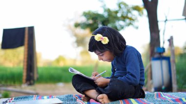 Öğrenci elinde kalemle parkta ödev yapıyor. Okul konseptine geri dönelim. Zavallı Çocuklar Yaşam Tarzı. Eğitim kavramı