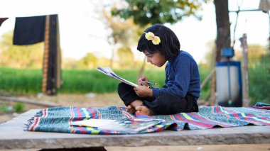 Zavallı küçük Hintli kız ev ödevi yapıyor. Çocuk yaz parkında kitap okuyor ve yazıyor. Çocukların parkta öğrenme, öğrenme, öğrenme kavramı.