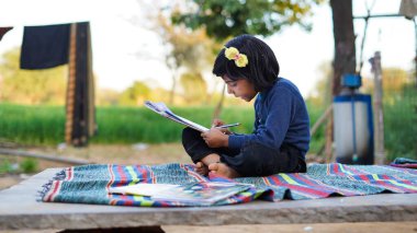 Tarım alanında oturan ve not defterine yazan zavallı küçük kızın yan görünüşü.