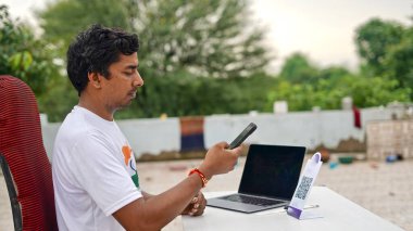 Genç Hintli adam cep telefonu ve laptop kullanarak faturaları ödüyor. QR kod taraması ve ödeme konsepti. Evden çalış.