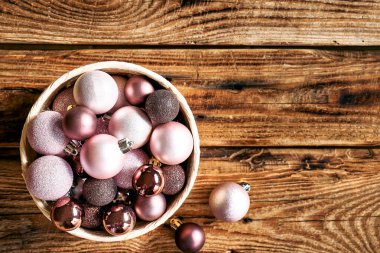 Ahşap arka planda, üzerinde fotokopi alanı olan sepetteki pembe Noel süsleri. Noel ve Yeni Yıl tebrik kartı. Asgari düzeyde. Düz yatıyordu.