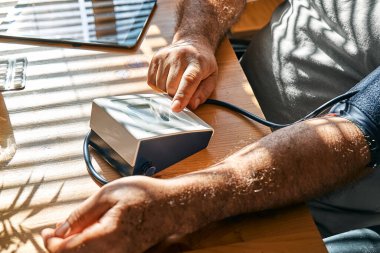 Middle aged man measuring his arterial blood pressure in the morning, using blood-pressure cuff to making check his health at home. Hypertension or hypotension issue concept.