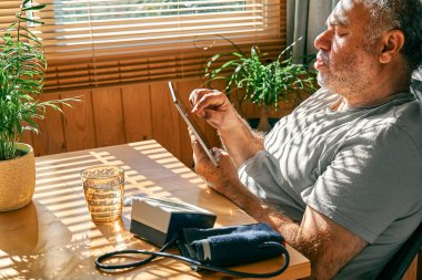Mature middle-aged overweight man in wireless headphones relaxing at home with his cat and guided meditation, listening to relaxing music on smartphone and meditating in lotus pose.