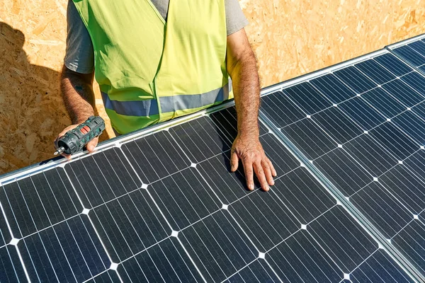Man\'s hands with drill installing stand-alone photovoltaic solar panel system on the rooftop of a house. Alternative energy,renewable energy source and power sustainable resources concept.