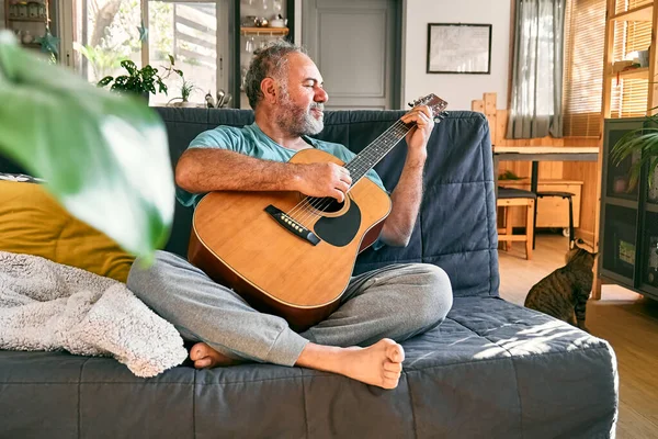 Middle Aged Bearded Man Playing Acoustic Guitar While Sitting Sofa — Stockfoto