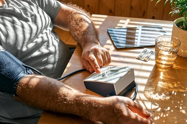 Middle aged man measuring his arterial blood pressure in the morning, using blood-pressure cuff to making check his health at home. Hypertension or hypotension issue concept.