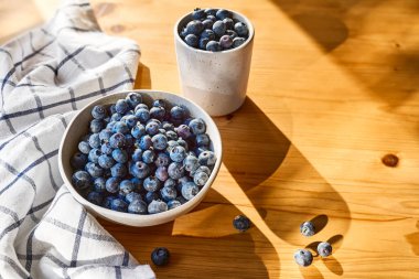 Fresh organic blueberries. Juicy ripe bilberry in white bowl on wooden table. Antioxidant and healthy eating concept.