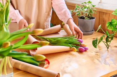 Woman florist making colorful tulips bouquet in flower shop. Flower delivery. Social media for small business.