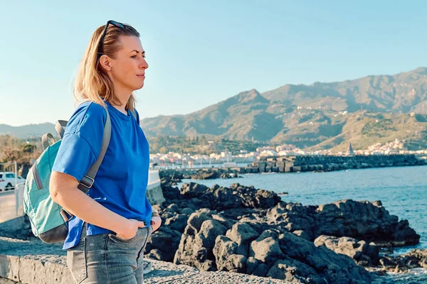 Sırt çantalı sarışın bir turist, deniz kenarında özgürlüğün tadını çıkarıyor. Dişi gezgin sakin doğada dinleniyor. Akıl sağlığı, sağlık, macera yolculuğu ve sağlıklı yaşam tarzı..