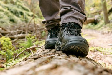 Gezgin adam dağ ormanlarında yürüyüş yapıyor. Ağaç kütüğünde yürüyen, dağ ayakkabısı giymiş insan ayaklarına yakın. Sağlık ve sağlıklı yaşam tarzı için doğada egzersiz ve uygunluk.