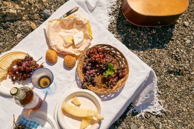 Yaz pikniği. Aperatifler, taze meyve, üzüm, sarı kavun, ekmek, peynir ve şarap sahildeki beyaz masa örtüsü üzerinde..