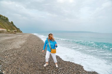 Açık mavi kapüşonlu çekici sarışın kadın kış kumsalında yürüyor. Seyahat ediyorum. Refah ve uyum kavramı. Doğayla birlik.