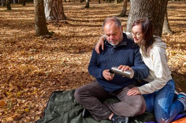 Orta yaşlı çift sonbahar ormanında termostan kahve içerken rahatlıyor. Sağlık ve sağlıklı yaşam için sonbahar doğasında zaman geçirmek. Özgürlük ve doğa konseptiyle birlik.