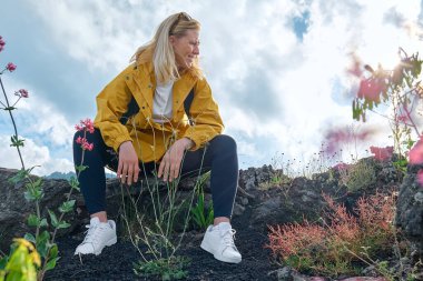 Avrupa 'nın en yüksek volkanı olan Etna' da yürüyüş. Gülümseyen genç kadın arka planda Etna Dağı 'nın kara kum lav-kayalık arazisindeki bitki örtüsü yakınlarındaki volkanik kayalarda oturuyor..