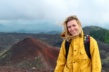 Avrupa 'nın en yüksek volkanı olan Etna' da yürüyüş. Sarı yağmurluk giymiş genç bir kadın rüzgarlı bir günde Etna Dağı 'nın panoramik manzarasının zirvesinde..