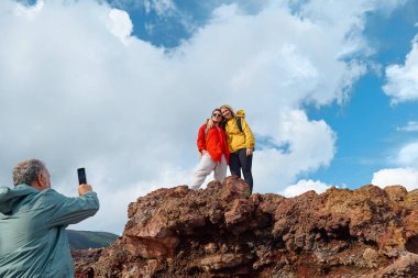 Avrupa 'nın en yüksek volkanı olan Etna' da yürüyüş. Arkaplanda bulutlu gökyüzü olan Etna Dağı 'nın panoramik manzarasının zirvesinde fotoğraf çeken bir grup arkadaş..