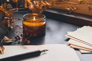 Samimi sonbahar hayat yaprakları, kağıt yaprakları, dolmakalem ve yanan mum pencere pervazında. Sonbahar evi dekorasyonu. Sıcak sonbahar havası.