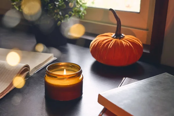 Cozy autumn still life with pumpkin, open books and candle on the windowsill. Autumn home decor. Cozy fall mood.