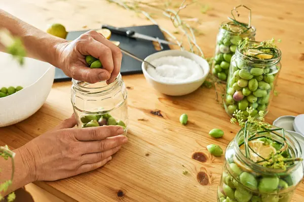 Kadın cam kavanozda mayalanmış zeytinleri limon dilimleri, yabani rezene ve konserve salamurasıyla hazırlıyor. Sonbahar sebzeleri konserve. Sağlıklı ev yemekleri. Hasatın korunması.