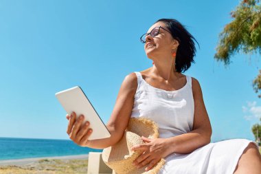 Kumsalda dijital tablet kullanan olgun bir kadın. Orta a