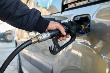 Hand of man driver holding fuel pump and refilling gasoline tank of car with fuel at gas station. clipart