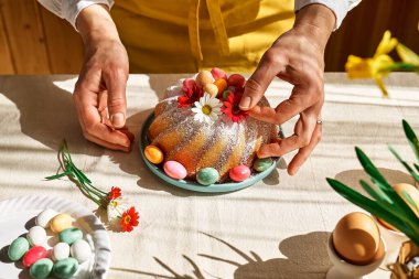Paskalya pastasını küçük renkli çikolata yumurtaları ve papatya çiçekleriyle süsleyen kadın elleri. Geleneksel paskalya pastası yapan isimsiz bir kadın ya da soslu tatlı ekmek. Paskalya hediyesi.
