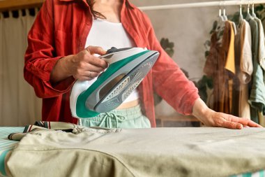 Tanımlanamayan orta yaşlı bir kadın evdeki ütü masasında çamaşır yıkıyor. Günlük ev hanımı rutini. Oda servisi kavramı.