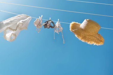 Beyaz kadın bikini mayosu yaz güneşli bir günde havayı kurutuyor. Mayo, pareo ve hasır şapka rüzgarda savruluyor. Yaz tatili konsepti, dinlenme, tatil.