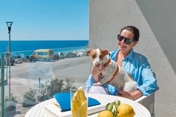 Kadın ve Jack Russell Terrier evcil hayvanı otelin balkonunda iletişim kuruyor. Avrupalı orta yaşlı güzel kadın ve köpeği birlikte vakit geçiriyorlar. Köpek dostu otel..