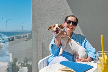 Gülümseyen Kadın ve Jack Russell Terrier 'ın otelin balkonundaki portresi. Avrupalı orta yaşlı güzel kadın ve köpeği birlikte vakit geçiriyorlar. Köpek dostu otel..