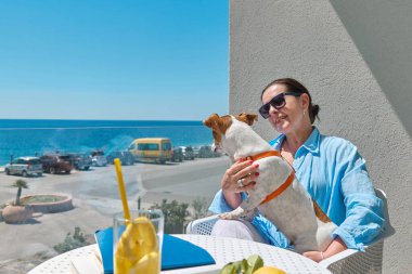 Kadın ve Jack Russell Terrier evcil hayvanı otelin balkonunda iletişim kuruyor. Avrupalı orta yaşlı güzel kadın ve köpeği birlikte vakit geçiriyorlar. Köpek dostu otel..