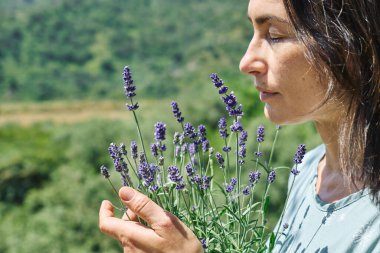 Kadın, kokulu lavanta çiçeklerinin kokusunu içine çekiyor. Doğal bitkisel tedavi yöntemleri. Alternatif tıp. Lavanta yağı. Aromaterapi.