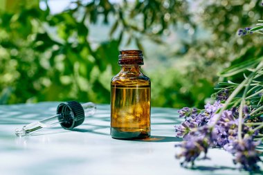 Doğal lavanta yağı ve mor lavanta çiçekli damlacık şişesi turkuaz yüzeyde doğa yeşili arka planda. Aromaterapi, alternatif tıp ve parfüm konsepti. Boşluğu kopyala