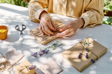 El yapımı hediye paketi yapan kadın geri dönüştürülmüş kağıt ve masada keten masa örtüsüyle kurutulmuş lavanta çiçekleri yapıyor. Doğal estetik..