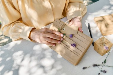 El yapımı hediye paketi yapan kadın geri dönüştürülmüş kağıt ve masada keten masa örtüsüyle kurutulmuş lavanta çiçekleri yapıyor. Doğal estetik..