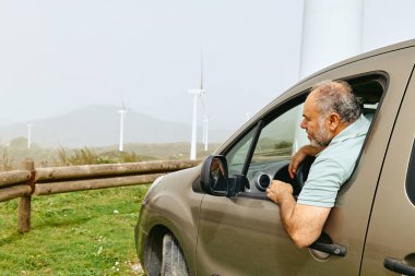 Rüzgâr tarlasında, dağ manzaralı bir arabadan bakan adam. Yeşil enerji konsepti. En iyi endüstriyel rüzgar santrali, rüzgar türbinleri rüzgar çiftliği ya da rüzgar parkında jenerasyon elektriği.