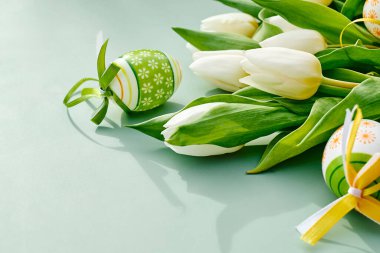 White tulips and easter eggs on green pastel background. Floral image with space for text for  Easter and other spring celebration. clipart