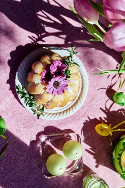 Paskalya pastası, masaya şeker ve papatya çiçekleri ile süslenmiş paskalya yumurtaları ve pembe masa örtüsünün üzerinde lalelerle. Geleneksel paskalya pastası ya da üzerine tatlı ekmek. Paskalya hediyesi.