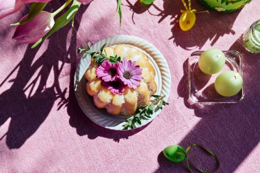 Paskalya pastası, masaya şeker ve papatya çiçekleri ile süslenmiş paskalya yumurtaları ve pembe masa örtüsünün üzerinde lalelerle. Geleneksel paskalya pastası ya da üzerine tatlı ekmek. Paskalya hediyesi.