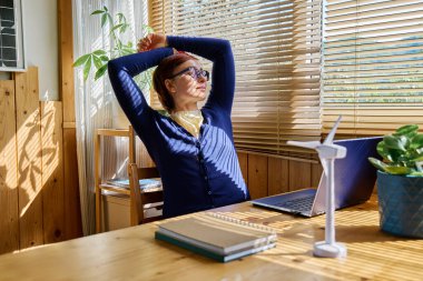 İş kadını dinleniyor ve pencereye bakıyor yenilenebilir enerji endüstrisinde güneşli bir günde ev ofisinde çalışıyor..